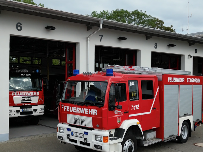 Ein rotes Feuerwehrauto vor dem Gerätehaus mit den Rolltoren der Feuerwehr